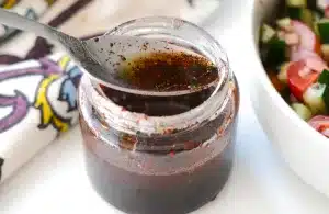 Spooning Persian Sumac Salad Dressing in a Bottle next to Shirazi Salad