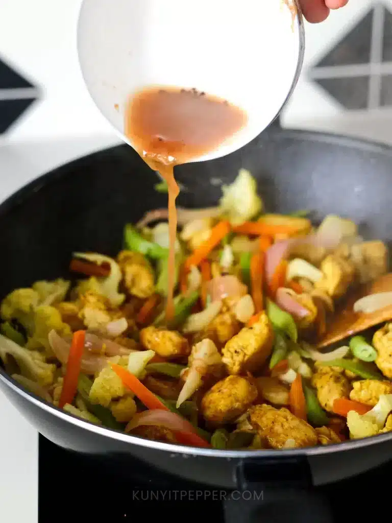 Pouring tamarind paste on turmeric chicken in a wok