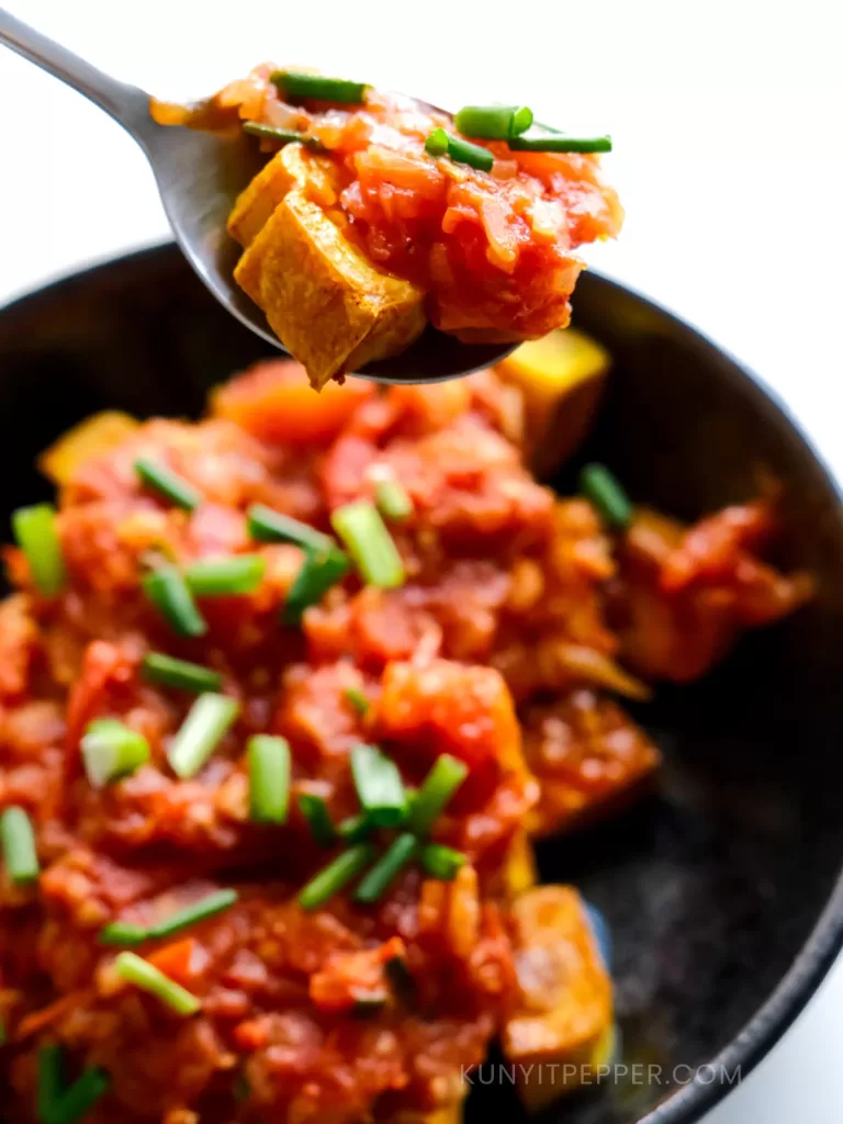 Spooning airfried tofu in tomato sauce with scallion
