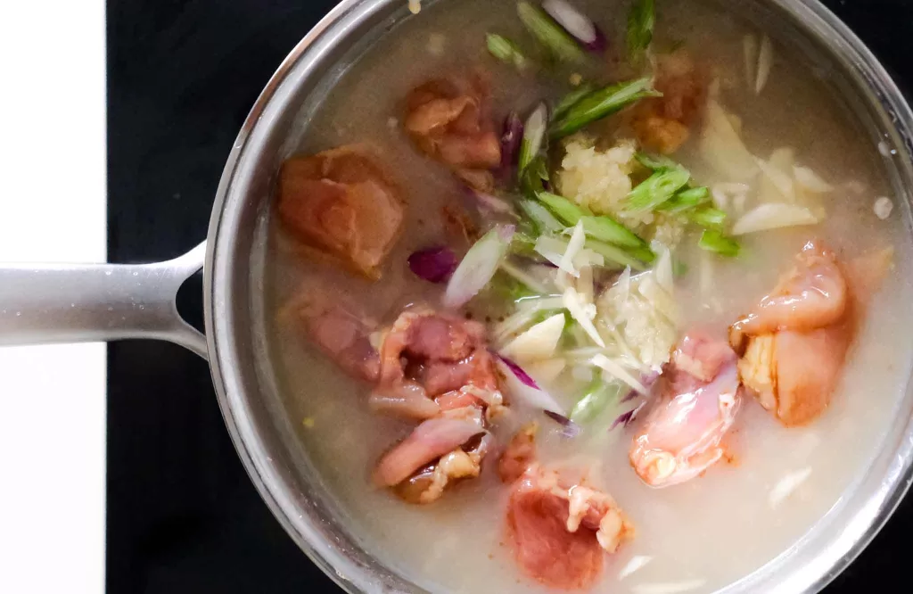 Adding marinated chicken and aromatics into a simmering congee
