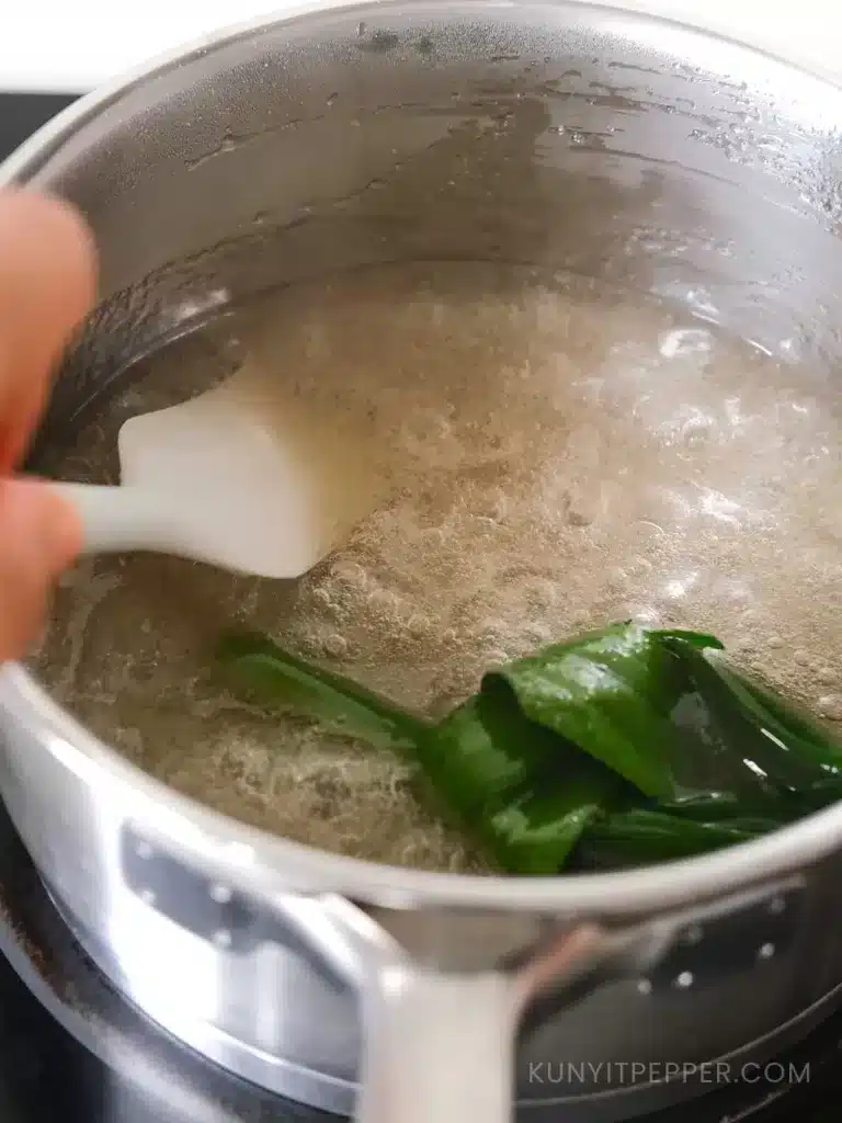 Stirring dissolved agar-agar and sugar with pandan leaf in a pot