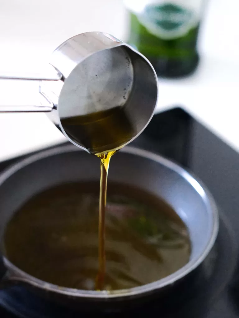 Pouring olive oil into a small skillet on the stovetop. Step to make chili oil with olive oil