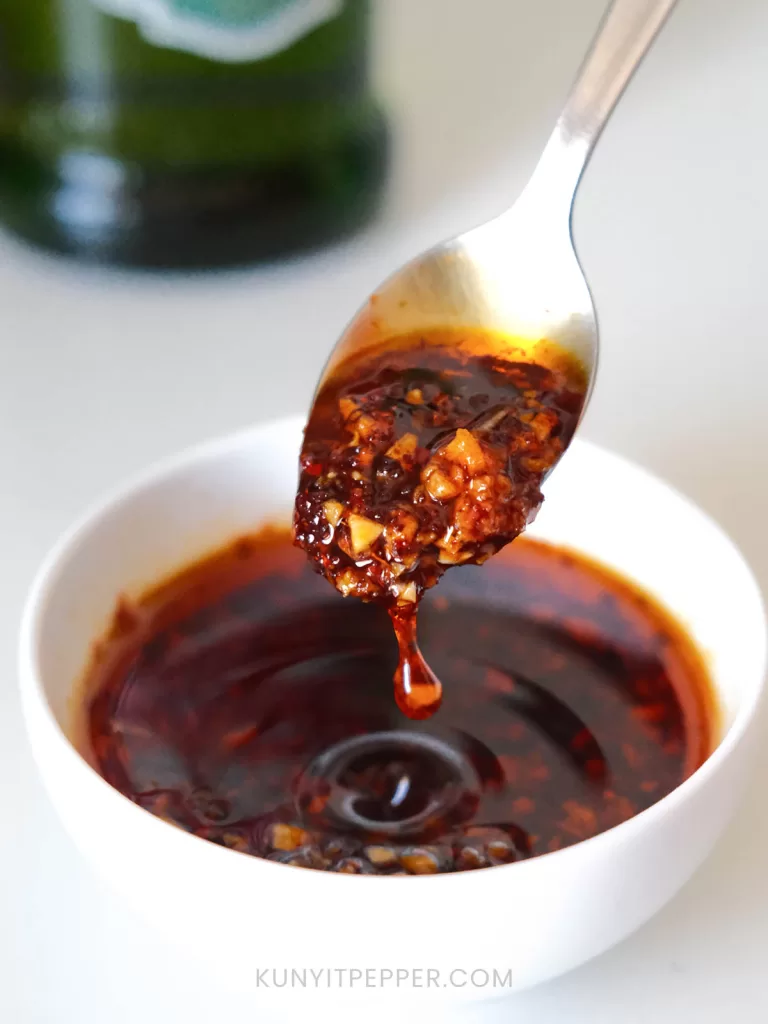 Spooning thick chili oil with olive oil from the bowl with the olive oil bottle behind