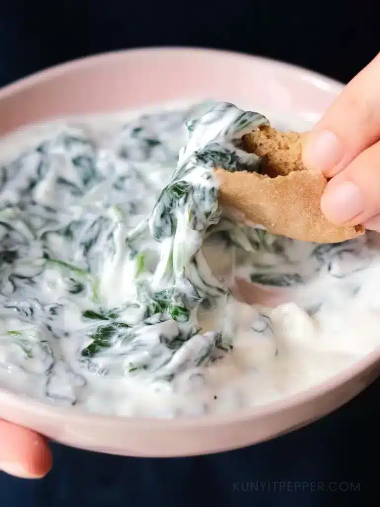 Dipping piece of pita bread into yogurt spinach dip
