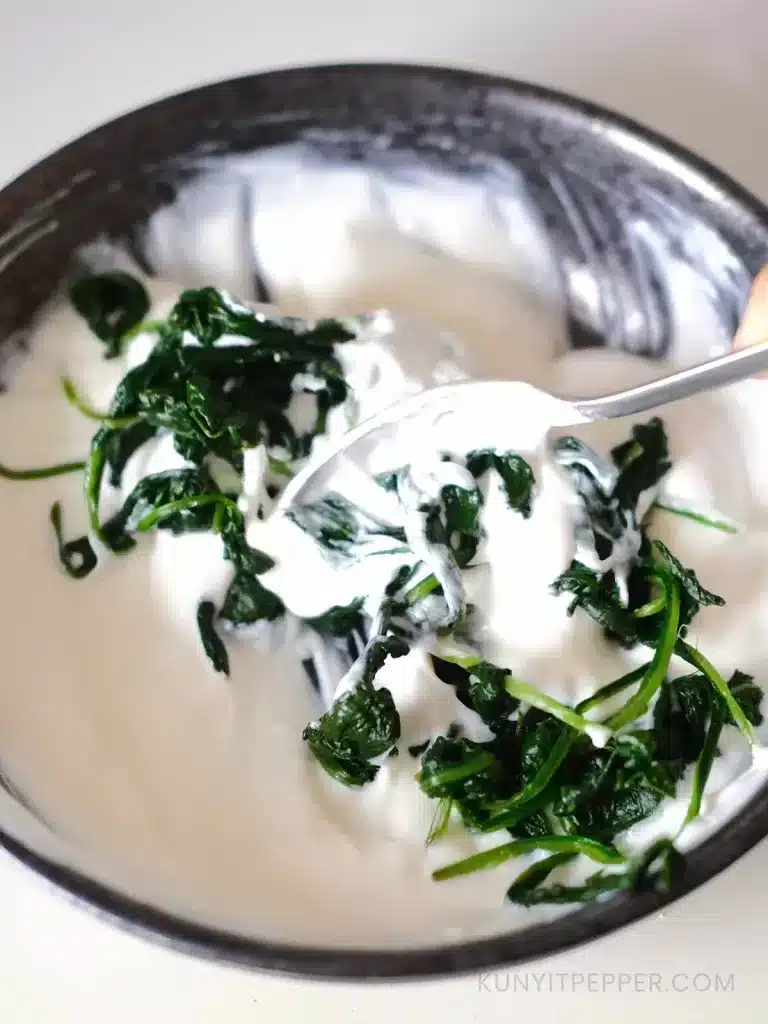 Stirring blanched spinach with garlicky yogurt in a bowl with spoon