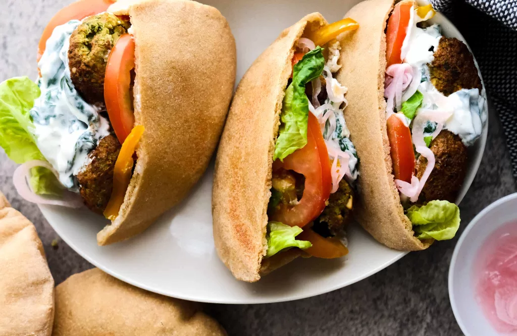 Three falafel sandwiches with creamy yogurt and spinach sauce