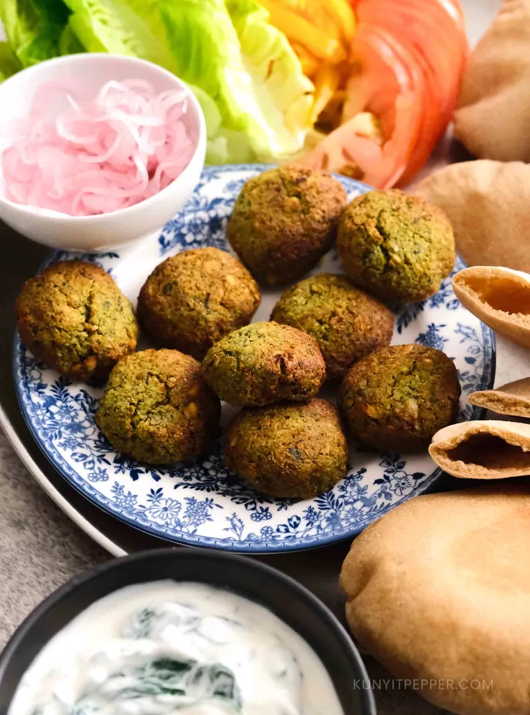 Airfried falafel, next to pita bread, vegetables, pickled onion, and yogurt spinach sauce