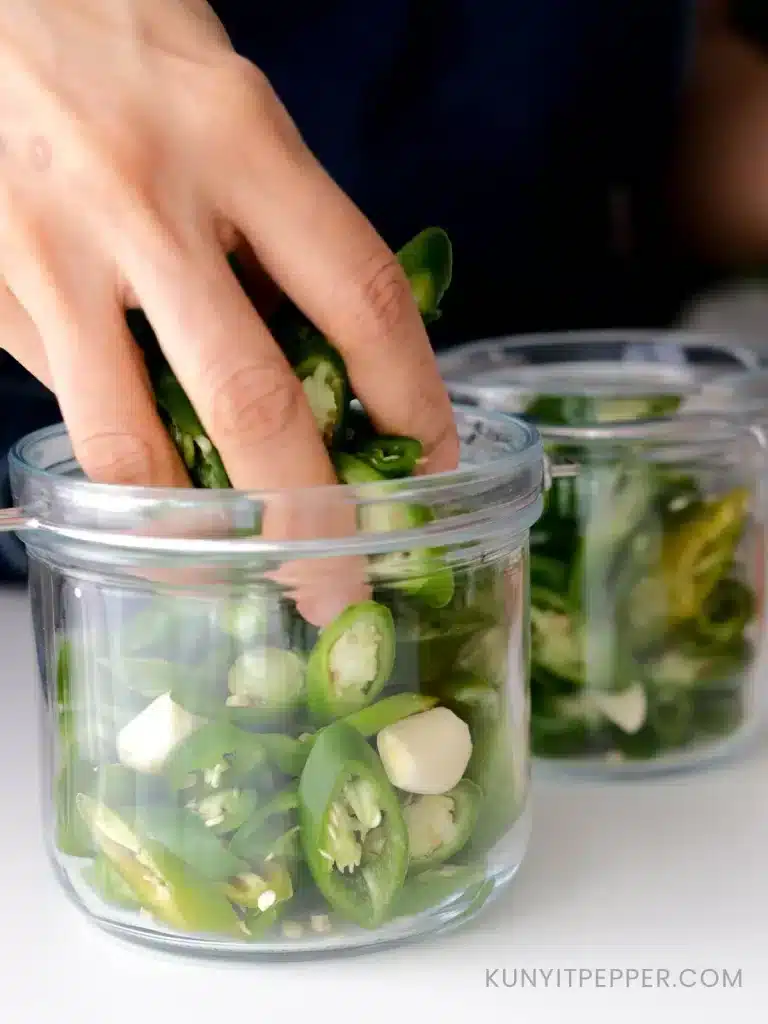 Transferring sliced green chilli into glass jar with hand