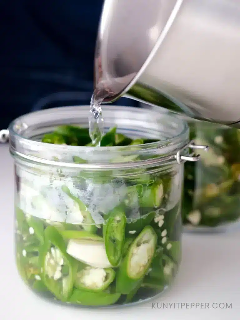 Pouring vinegar brine onto a jar of sliced green chillis to make pickled green chilli